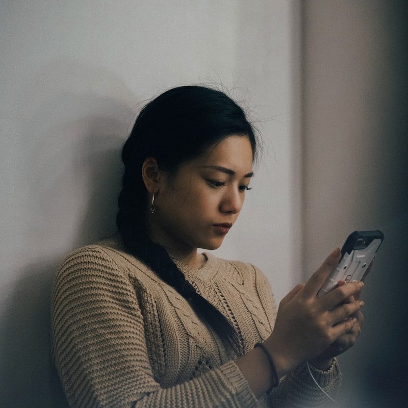 woman leaning back on white wall and using smartphone