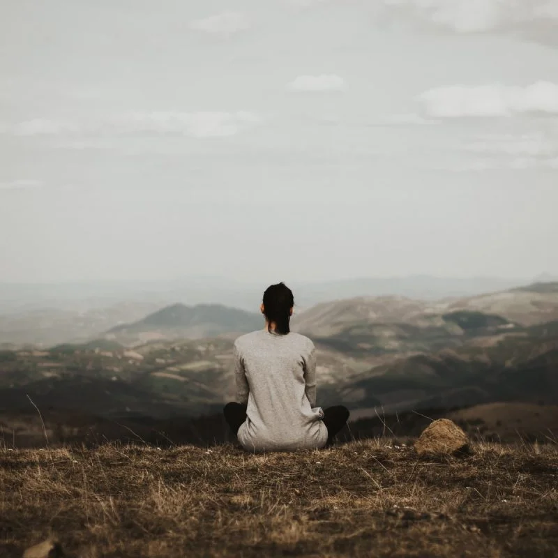 woman sitting on cliff overlooking mountains during daytime