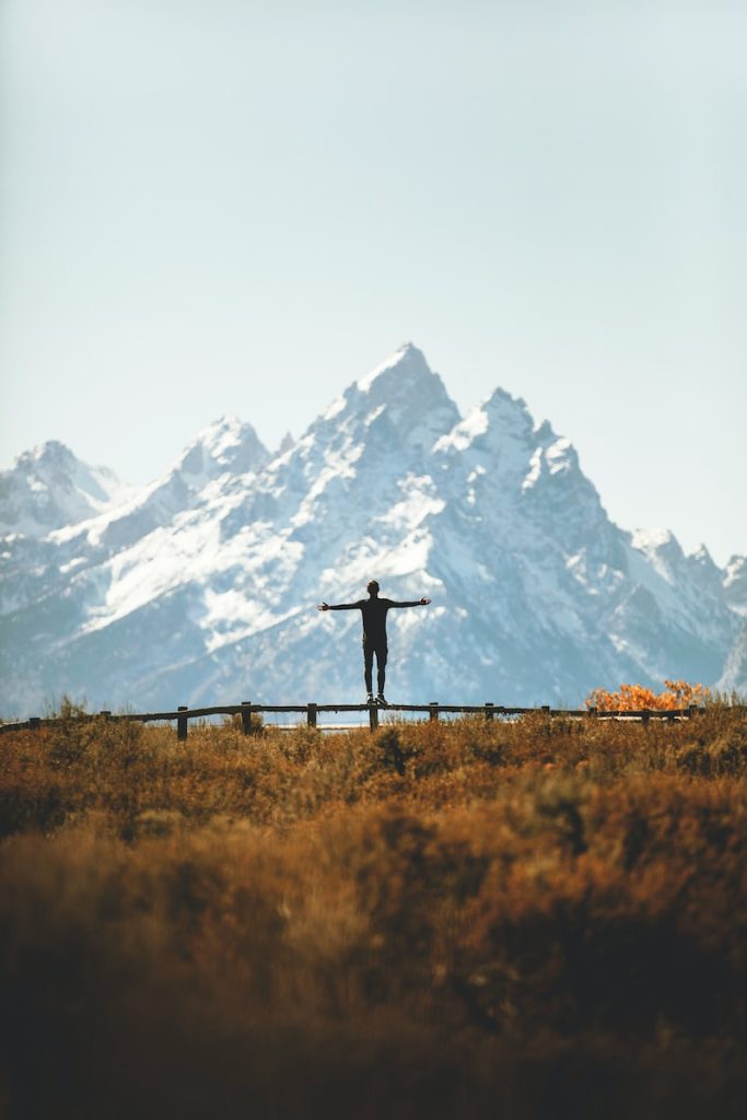 man standing on fence overlooking mountain range