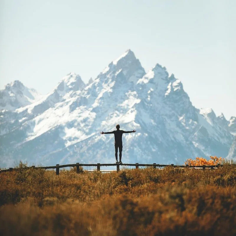 man standing on fence overlooking mountain range