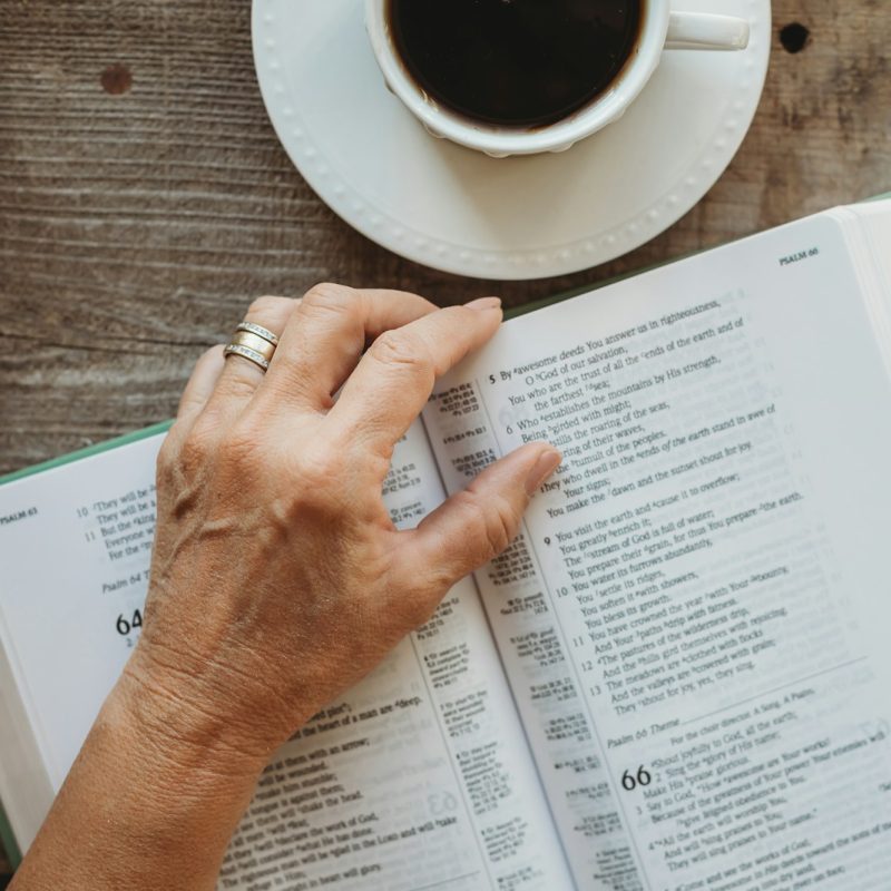 a person's hand resting on an open book next to a cup of coffee