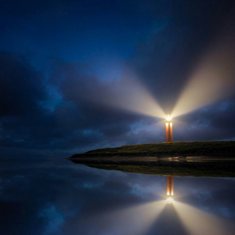 lighted brown lighthouse beside body of water